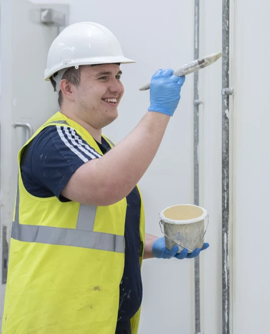 Smiling student in hard hat applying paint with a brush to a wall Smiling student in hard hat applying paint with a brush to a wall